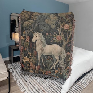 May include: A tapestry throw blanket featuring a white unicorn standing in a forest with colorful flowers and trees. The unicorn has a long flowing mane and tail.