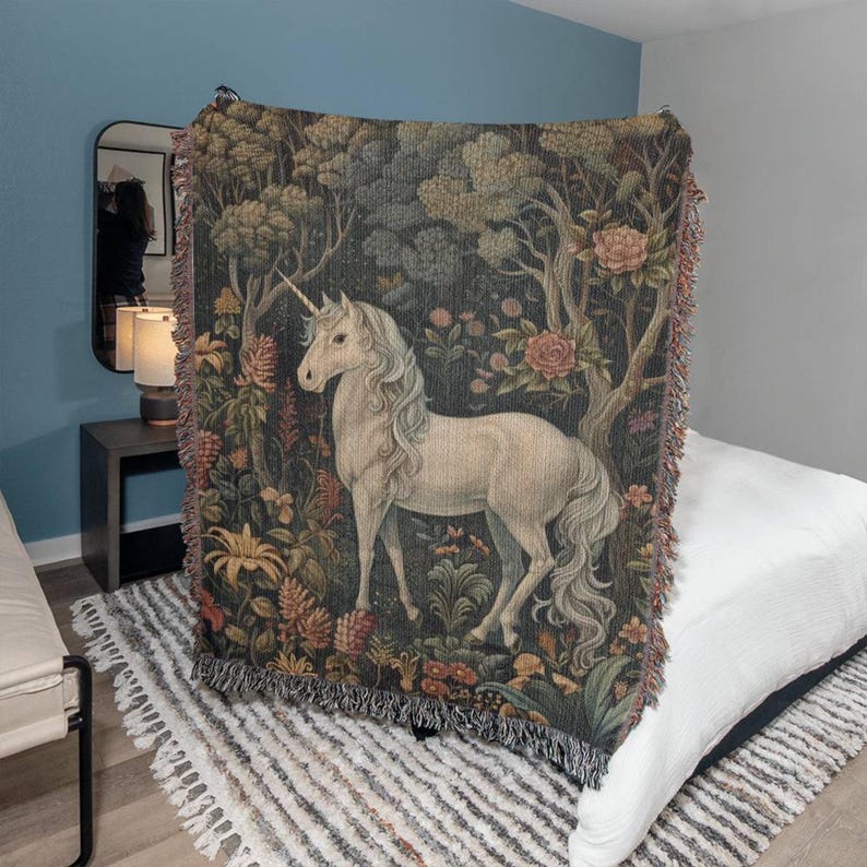 May include: A tapestry throw blanket featuring a white unicorn standing in a forest with colorful flowers and trees. The unicorn has a long flowing mane and tail.