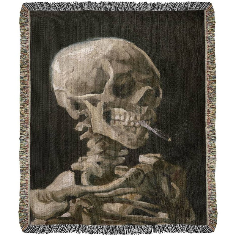 May include: A woven tapestry featuring a detailed depiction of a human skull with a cigarette in its mouth. The skull is rendered in a realistic style with visible teeth and bone structure. The background is a dark, almost black, color.