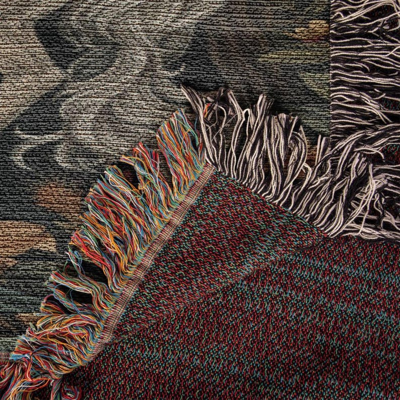 May include: Close-up of a woven tapestry with a colorful fringe. The tapestry has a dark brown background with a pattern of red, blue, and green threads.