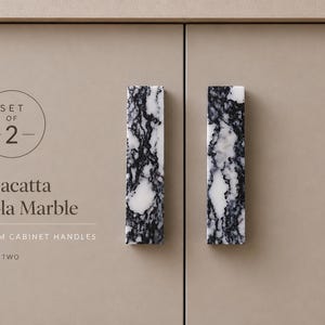 May include: A set of two rectangular cabinet handles made of Calacatta Viola marble with a distinct black and white veined pattern. The handles measure 160mm in length. The text on the image reads: Set of 2, Calacatta Viola Marble, 160mm cabinet handles.