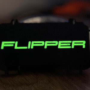 May include: A black device with the word "FLIPPER" in green lettering on the front.