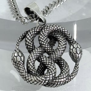 以下が含まれることがあります： 詳細なヘビのデザインが施されたシルバーカラーのペンダントネックレス。ペンダントは、テクスチャ加工された鱗とヘビの頭を持つ、円形のパターンで絡み合った2匹のヘビを描いています。ネックレスはカーブチェーンです。