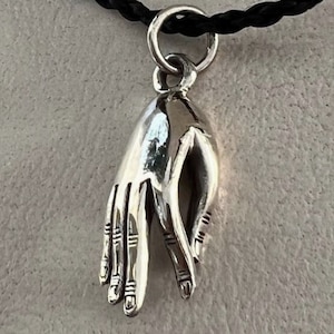 Puede incluir: Collar con colgante de plata que presenta un gesto de mano detallado, posiblemente un símbolo de paz o bendición.