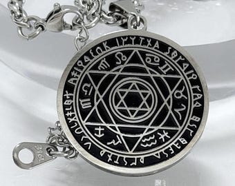May include: A silver-colored pendant necklace featuring a circular pendant with a black center. The pendant has a star design in the center and is surrounded by symbols and text. The necklace chain is also silver-colored.