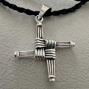 May include: A silver Celtic knot pendant necklace with a braided design. The pendant is in the shape of a cross with four arms that are intertwined.