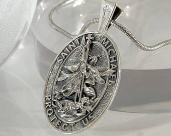 Può includere: Collana con pendente ovale color argento raffigurante San Michele. Il pendente reca l'iscrizione "SAINT MICHAEL PROTECT US". La collana ha una catena sottile.