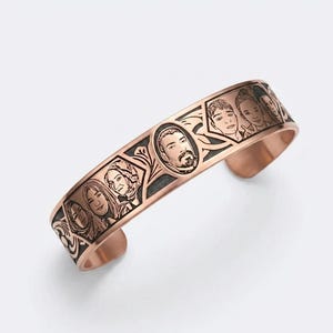 May include: A copper-toned metal cuff bracelet featuring a series of engraved portrait illustrations of various individuals within decorative geometric frames, set against a dark, recessed background that highlights the detailed line work.