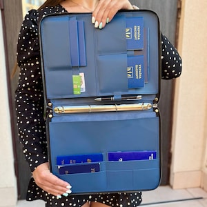 May include: A blue zippered document organizer featuring multiple interior pockets, a central metal ring binder mechanism, and a pen holder. The organizer contains several blue passports with the text UKRAINE PASSPORT printed in gold on the covers.