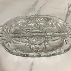 Puede incluir: Un plato de servir de vidrio transparente dividido con un patrón de estrella. El plato tiene dos secciones y un asa en el centro.