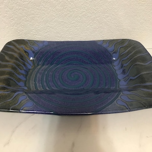 May include: A blue and green ceramic serving dish with a spiral design. The dish has a glazed finish and a slightly raised rim.