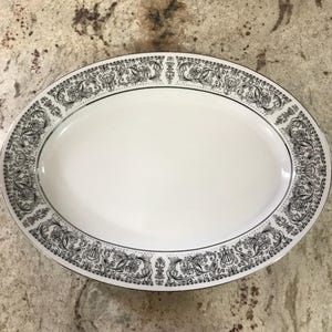 Puede incluir: Plato ovalado blanco para servir con un diseño floral negro y plateado alrededor del borde.