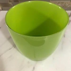 Puede incluir: Un cuenco verde brillante con forma redondeada. El cuenco está vacío y se encuentra sobre una superficie blanca. El interior del cuenco es de color verde brillante.