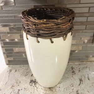 以下が含まれることがあります： 白磁の壺に、籐で編まれた蓋がついたもの。明るいグレーのカウンタートップの上に置かれている。