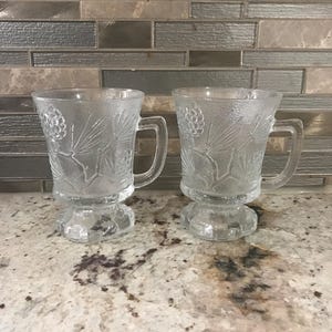 Two Indiana Glass Clear Coffee Thick Heavy With Pine Cone & Branches Design Footed Pedestal Pair Of Mugs (4 1/2 Inches H’ X 3 1/2 Inches W’)