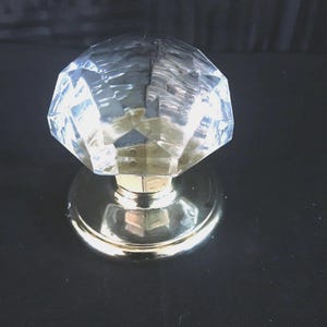 May include: A clear glass door knob with a faceted design and a brass base.