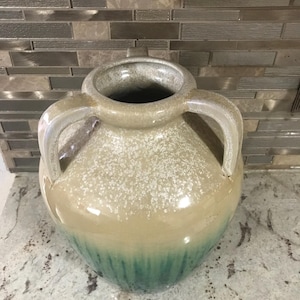 May include: A ceramic vase with two handles, a speckled beige body, and a green glaze at the bottom.