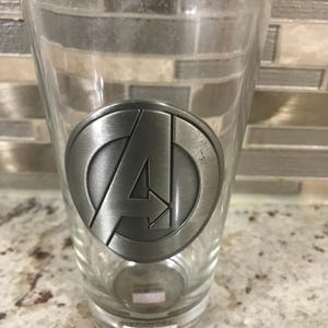 Vaso de vidrio grueso coleccionable con medallón de metal en 3D de Avenger con temática de Marvel (6 pulgadas de alto x 3 1/2 pulgadas de ancho)