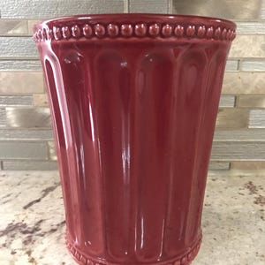 Puede incluir: Un porta cubiertos de cerámica rojo con un borde de cuentas y nervaduras verticales.