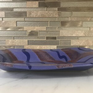 May include: A blue and purple ceramic serving dish with a wavy design. The dish is rectangular and has a slightly uneven edge.