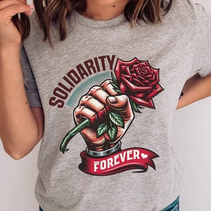May include: Gray t-shirt with a graphic of a fist holding a red rose with green leaves. The text "Solidarity Forever" is printed on a red ribbon.