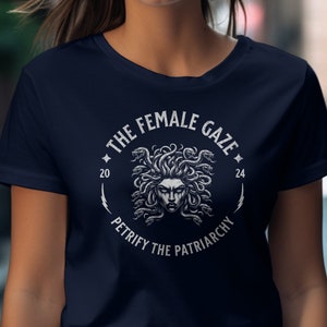 Puede incluir: Una camiseta azul marino con un gr&aacute;fico blanco de la cabeza de Medusa rodeada de serpientes. El gr&aacute;fico incluye el texto "The Female Gaze" y "Petrify the Patriarchy".