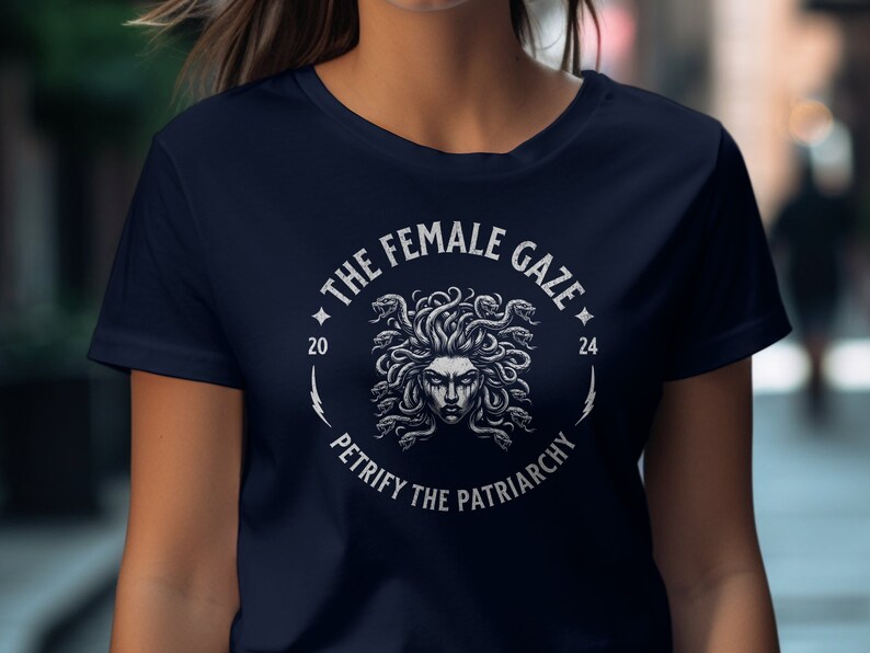 Puede incluir: Una camiseta azul marino con un gr&aacute;fico blanco de la cabeza de Medusa rodeada de serpientes. El gr&aacute;fico incluye el texto "The Female Gaze" y "Petrify the Patriarchy".