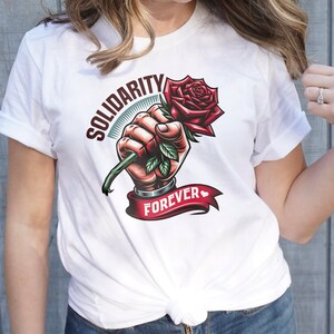 May include: White t-shirt with a graphic of a hand holding a red rose with green leaves. The text "Solidarity Forever" is printed on the shirt.