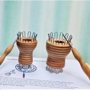Könnte beinhalten: Zwei Holz-Stricknadeln mit Metallnadeln und einer Holz-Stricknadel. Die Stricknadeln sind aus hellbraunem Holz mit dunkelbraunen Streifen. Die Nadeln sind silberfarben. Die Stricknadeln liegen auf einer weißen Oberfläche. Der Text auf der Oberfläche lautet: "Bitte ganz locker stricken!"