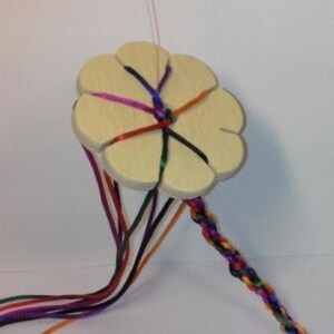 Könnte beinhalten: Ein hölzerner, blumenförmiger Webrahmen mit acht Fäden aus buntem Garn, der zum Herstellen von Freundschaftsarmbändern verwendet wird.