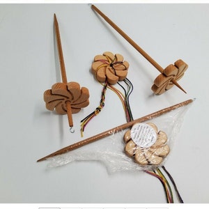 May include: Three wooden spinning wheels with a flower design. The wheels are made of light brown wood and have a spiral pattern. The wheels are attached to wooden spindles. The spindles are different lengths. The wheels are on a white surface.