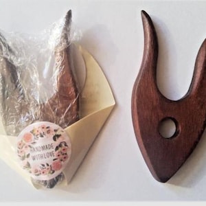 Könnte beinhalten: Zwei hölzerne Stricknadelhalter, einer in Klarsichtfolie verpackt mit einem Blumenaufkleber, auf dem "Handmade with Love" steht, der andere ist aus dunkelbraunem Holz mit einem Loch in der Mitte.