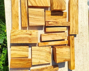 May include: A collection of various-sized olive wood blocks, showcasing natural grain patterns and warm tones. Some blocks have dimensions written on them in inches. Ideal for woodworking projects or crafts.