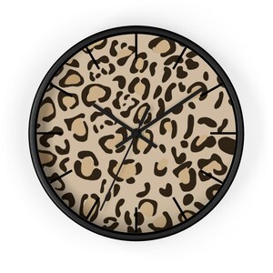 May include: Round wall clock with a black frame and a leopard print face. The clock features black hands and hour markers, and the leopard print has a tan background with brown spots. A decorative item for home decor.