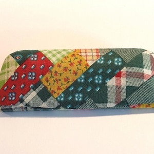 May include: A colorful eyeglasses case with a patchwork design. The case features a variety of fabrics in red, green, yellow, and blue, arranged in a diagonal pattern. The case is rectangular with rounded ends.