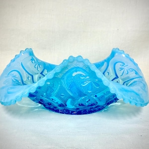 May include: A bright blue opalescent glass bowl with a ruffled, beaded edge. The exterior features a molded relief pattern of stylized floral and scroll motifs with a textured finish, creating a translucent appearance throughout the piece.