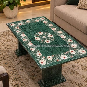 May include: A rectangular green marble coffee table featuring a central floral inlay and a matching floral border pattern made of white and red stone. The surface displays the text AZANINTERNATIONAL in white lettering across the centre.