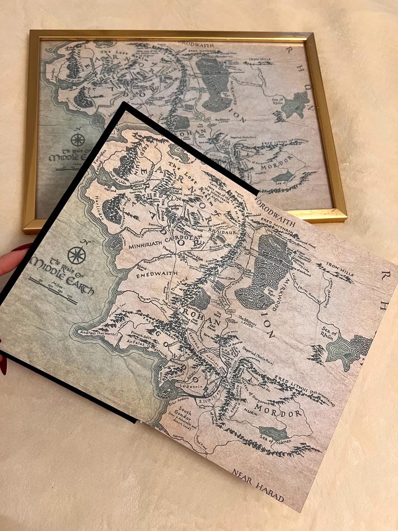May include: A vintage-style map of Middle-earth from The Lord of the Rings, featuring the text "The Realm of Middle-earth" and "The Lost Realm of Numenor". The map is printed on a cream-colored paper with brown and black ink.