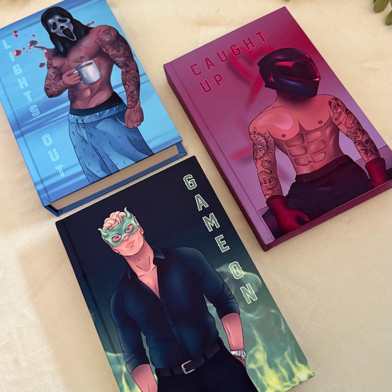 May include: Three hardcover books with illustrated covers. The blue book features a masked figure holding a mug with the text LIGHTS OUT. The magenta book shows a helmeted figure with the text CAUGHT UP. The black book shows a masked figure with GAME ON.