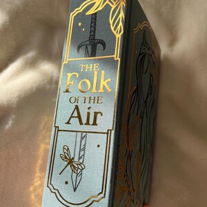 Puede incluir: Un libro de tapa dura azul con letras doradas e ilustraciones. El t&iacute;tulo es "The Folk of the Air".