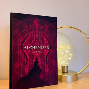Puede incluir: Un libro de tapa dura titulado "ALCHEMISED" de Senlinyu. La portada presenta una ilustración rojo oscuro con una silueta y elementos arquitectónicos. A la derecha hay una lámpara dorada decorativa con una bombilla encendida.