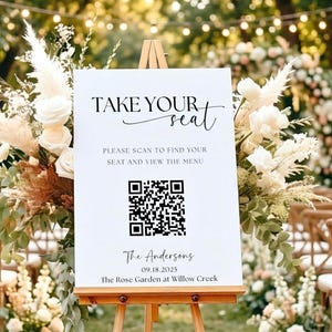 May include: A white sign on a wooden easel with the text "TAKE YOUR seat". Below, it reads "PLEASE SCAN TO FIND YOUR SEAT AND VIEW THE MENU". A QR code is present, followed by names, a date, and a location.