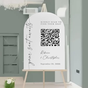 May include: White wedding sign with an arched top, displayed on a wooden easel. The sign features the text "your seat awaits" and "KINDLY SCAN TO FIND YOUR SEAT". A QR code and names "Rebecca & Christopher" are also displayed.