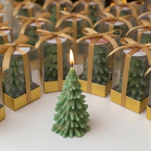 Könnte beinhalten: Eine brennende grüne Weihnachtsbaumkerze mit goldenen Glitzerakzenten steht vor mehreren Geschenkboxen mit ähnlichen baumförmigen Kerzen. Die Kerzen stehen auf einer weißen Oberfläche, mit einem verschwommenen Weihnachtsbaum im Hintergrund.