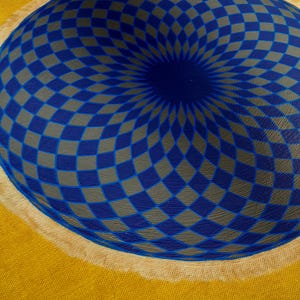 May include: A blue and gray checkered pattern painted on a canvas, creating a 3D effect of a sphere. The background is a solid yellow color.