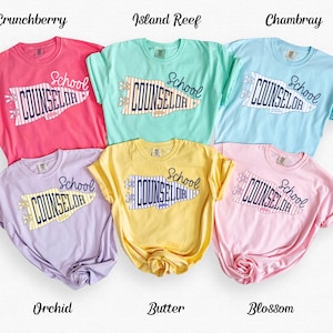 May include: Six short-sleeved t-shirts in colours Crunchberry, Island Reef, Chambray, Orchid, Butter, and Blossom. Each shirt features a graphic of a pennant flag with the text School COUNSELOR in dark blue, accented with small flower icons.