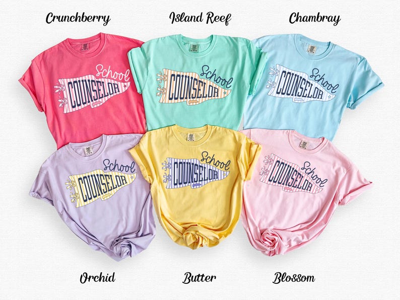 May include: Six short-sleeved t-shirts in colours Crunchberry, Island Reef, Chambray, Orchid, Butter, and Blossom. Each shirt features a graphic of a pennant flag with the text School COUNSELOR in dark blue, accented with small flower icons.