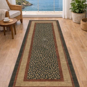 May include: Rectangular area rug with a leopard print center, framed by a tan border and a dark green outer edge. The rug is placed on a hardwood floor, with a view of the ocean through a large window.