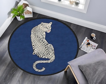 May include: A round blue rug with a white and black leopard print design. The leopard is facing away from the viewer and is sitting on its haunches.