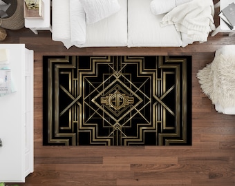 May include: A black and gold geometric rug with an Art Deco design. The rug features a large central diamond shape with a monogram in the center. The monogram is surrounded by a series of concentric squares and triangles.